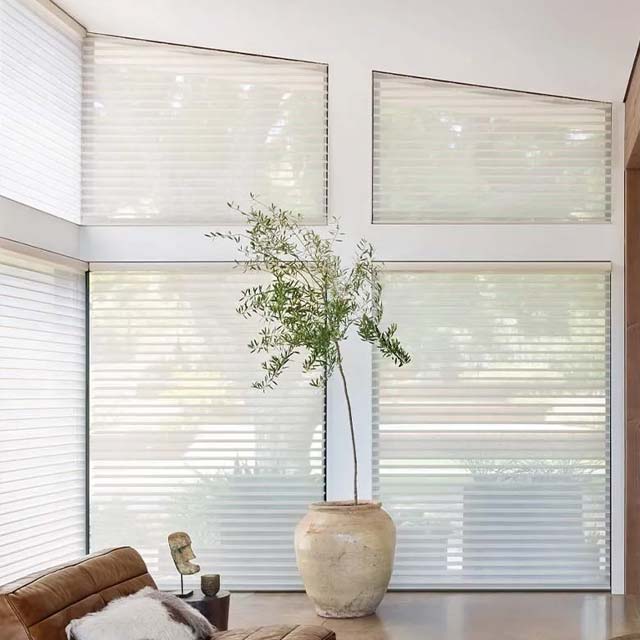 white sheer window blinds angled windows in living room with large plant and leather chair