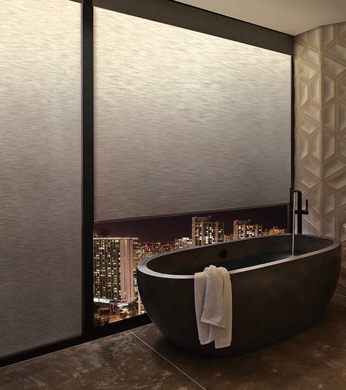 bathroom with illuminated roller shades at night by bathtub