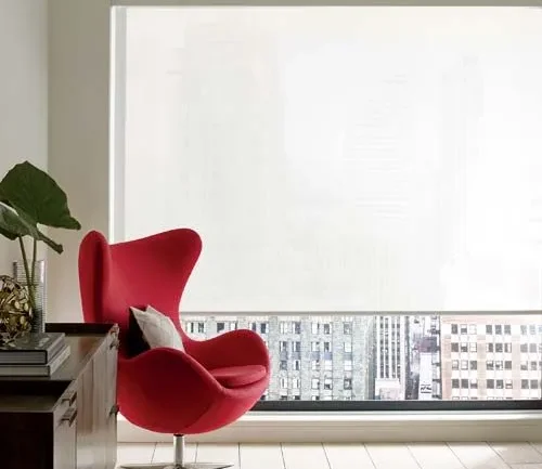 white screen shade infront of large window with red chair